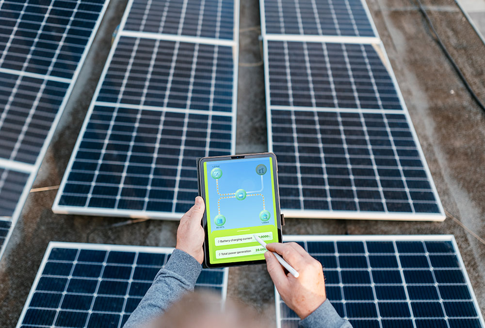 Primo piano di mani che utilizzano un tablet e una stylus per monitorare un impianto fotovoltaico sul tetto. Lo schermo del tablet mostra un'app di gestione energetica con dati di generazione e ricarica della batteria. L'immagine rappresenta il servizio di diagnosi guasti fotovoltaico senza sopralluogo a Cagliari di Energisolar Sardegna, che utilizza tecnologie avanzate come il monitoraggio delle curve I-V per analizzare a distanza lo stato dei pannelli,