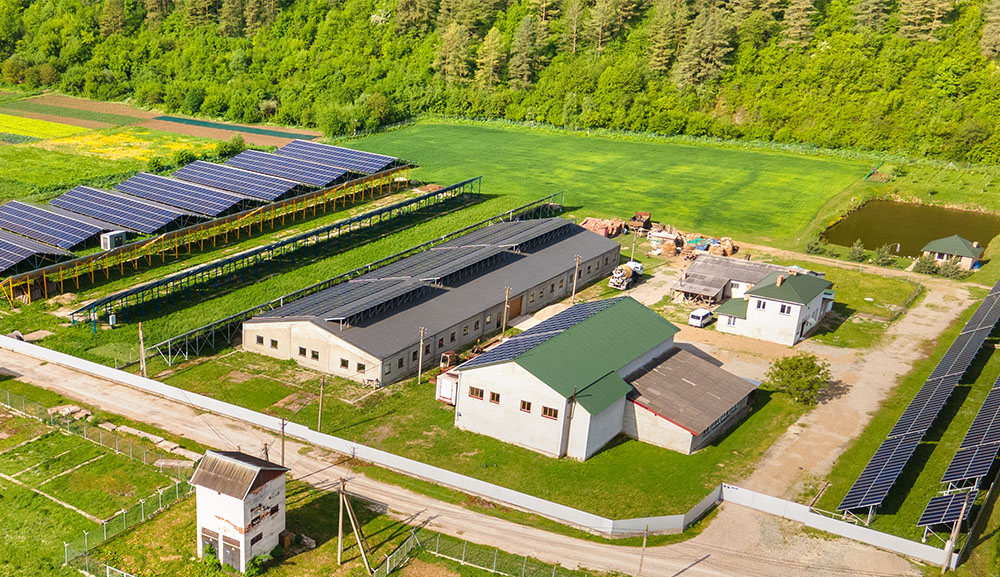 Veduta aerea di un'azienda agricola in Sardegna con impianto agrivoltaico, pannelli solari installati sui tetti dei capannoni e strutture sopraelevate sui campi coltivati.